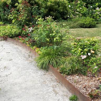 Bordure de jardin en acier corten brut 2 ml délimitant une allée pavée et un massif floral verdoyant