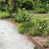 Bordure de jardin en acier corten brut 2 ml délimitant une allée pavée et un massif floral verdoyant